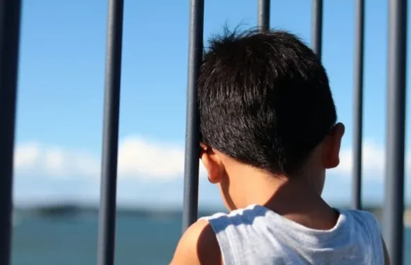 柵越しに海を眺める後ろ姿の少年