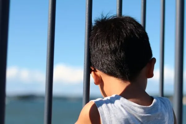 柵越しに海を眺める後ろ姿の少年