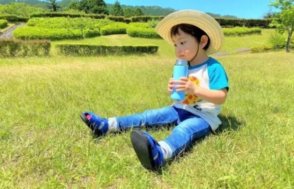 麦わら帽子で水筒の水を飲む男の子