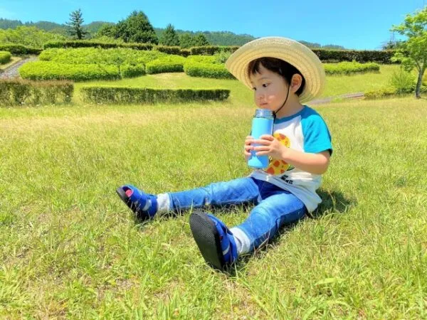 麦わら帽子で水筒の水を飲む男の子