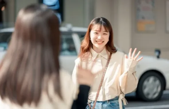 街中で笑顔で手を振る女性と話す女性の後ろ姿