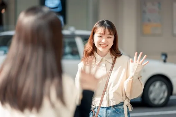 街中で笑顔で手を振る女性と話す女性の後ろ姿