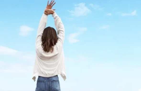 青空に向かって両手を伸ばす女性の後ろ姿
