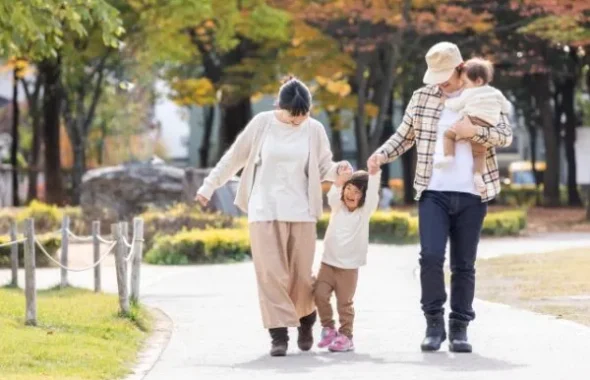 紅葉の公園を手をつないで歩く家族4人