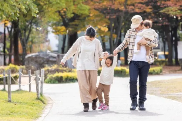 紅葉の公園を手をつないで歩く家族4人