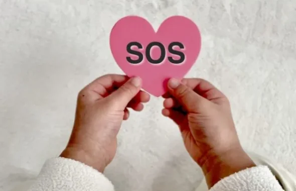 「SOS」と書かれたハート型の紙を持つ手