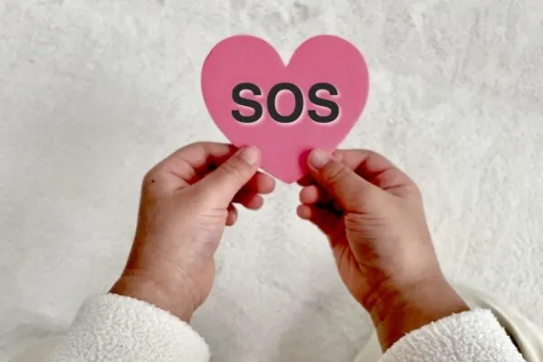 「SOS」と書かれたハート型の紙を持つ手