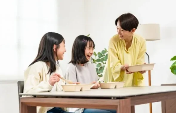 食卓で食事をしながら笑う母親と娘たち