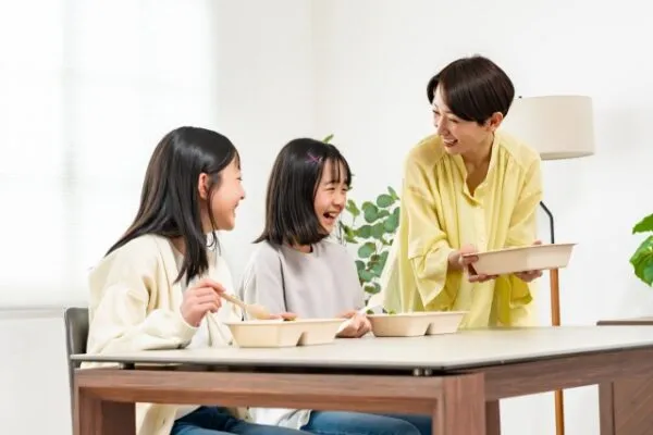食卓で食事をしながら笑う母親と娘たち