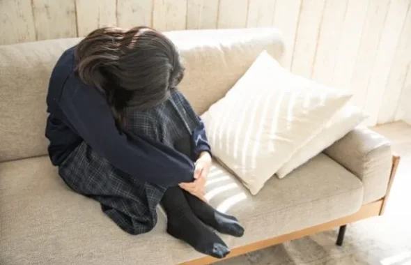 ソファでうずくまり体調不良の様子の女子学生