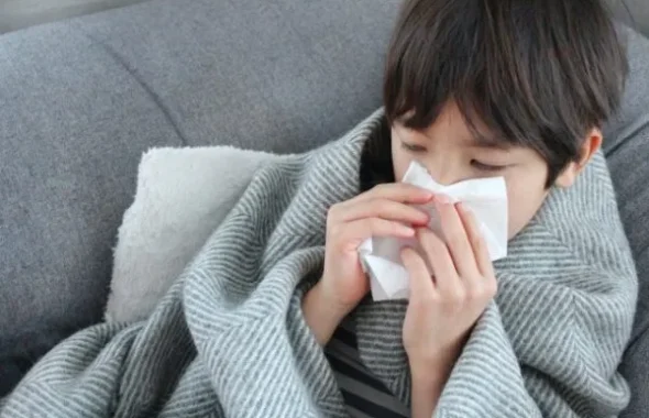 毛布にくるまり鼻をかむ体調不良の男の子