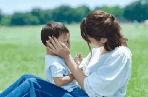 芝生の上で子供の顔にそっと触れる母親
