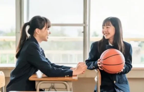 教室でバスケットボールを持ち談笑する制服姿の女子学生2人
