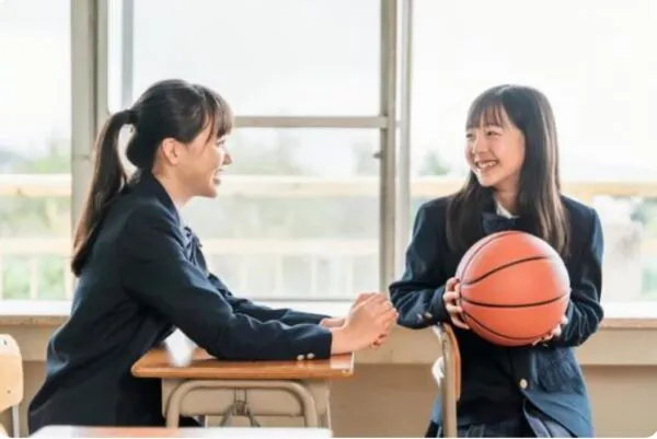 教室でバスケットボールを持ち談笑する制服姿の女子学生2人