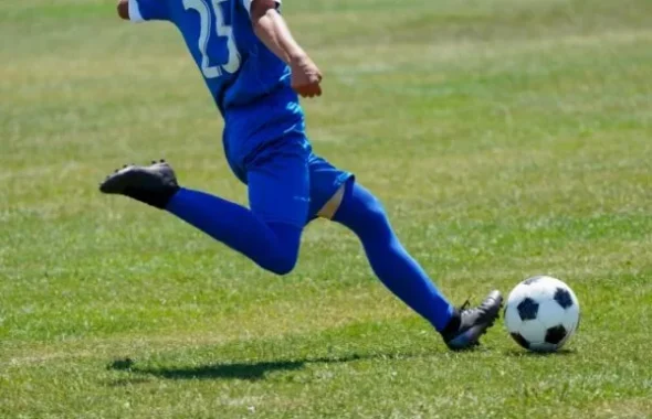 サッカーボールを蹴るユニフォーム姿の選手の脚