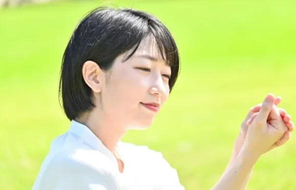 草原で穏やかな表情で手を合わせる女性
