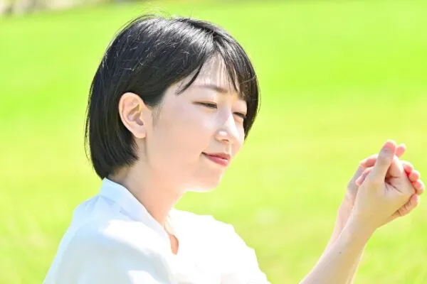 草原で穏やかな表情で手を合わせる女性